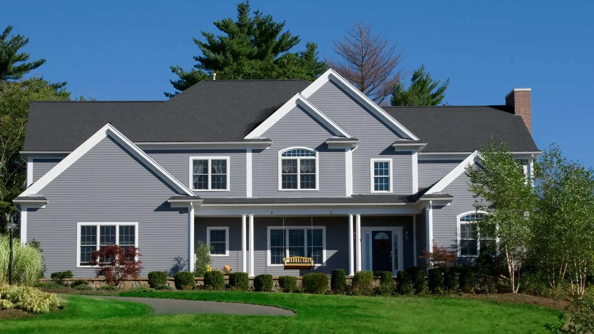 Two-story grey home with white trim, multiple gables, and a porch swing under a covered front entryway.