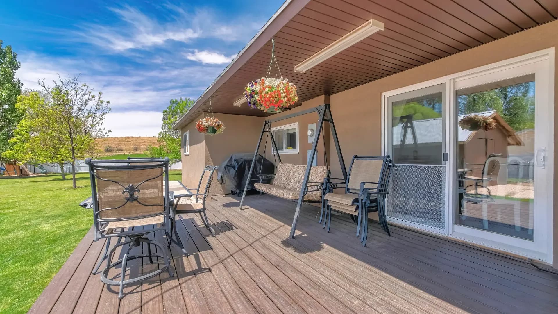 Outdoor wooden deck with patio furniture, a freestanding porch swing, and a white sliding glass door leading into the house.