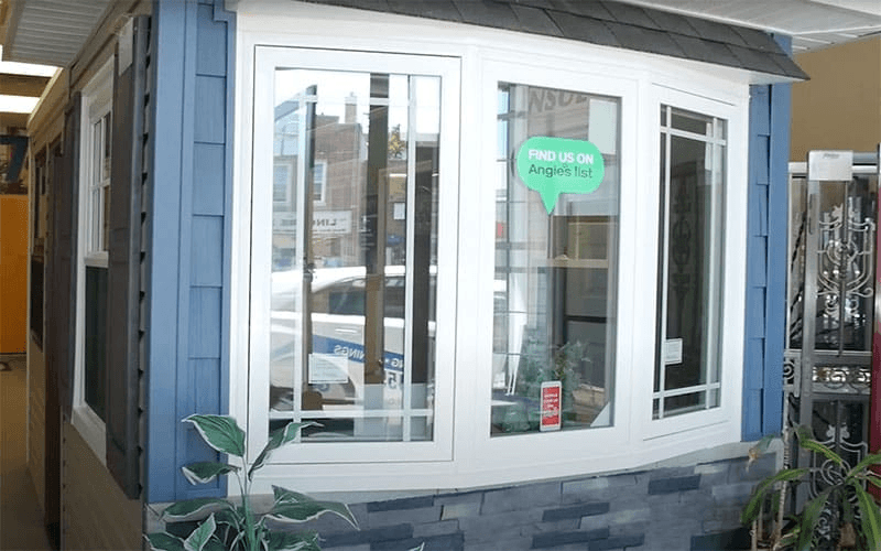 White bay window display with grid patterns and a blue siding frame inside a showroom.