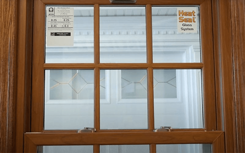 Close-up of a wood-grain double-hung window with six-pane grilles and Energy Star certification stickers.