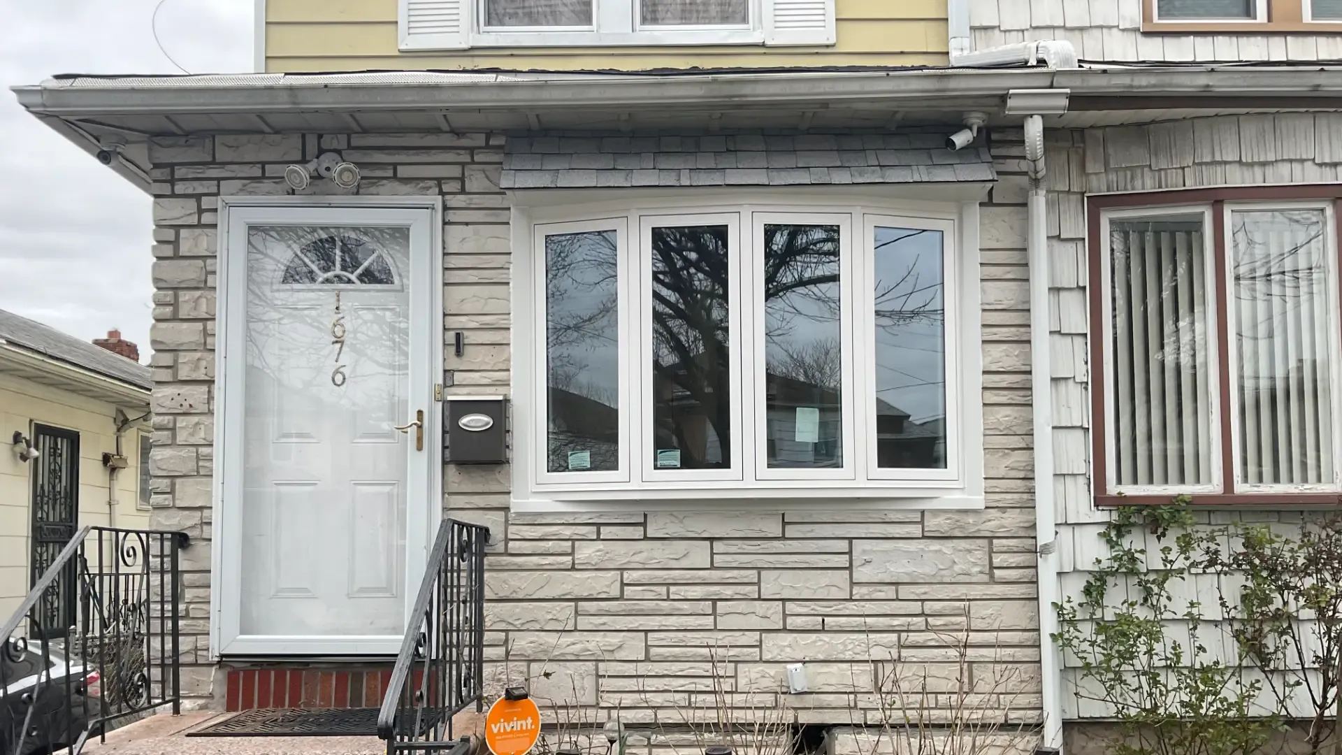Four-lite white bow window installed on a light-colored faux stone exterior wall next to a white storm door.
