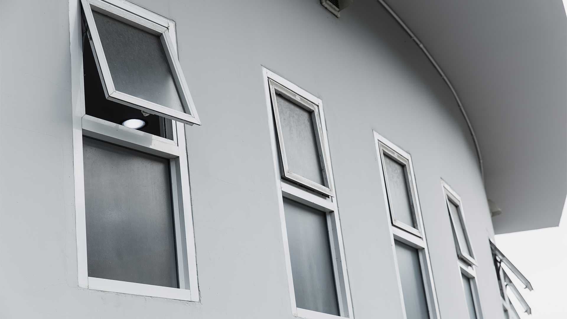 Line of white-framed awning windows, with one opened, set into a modern light-grey curved wall.