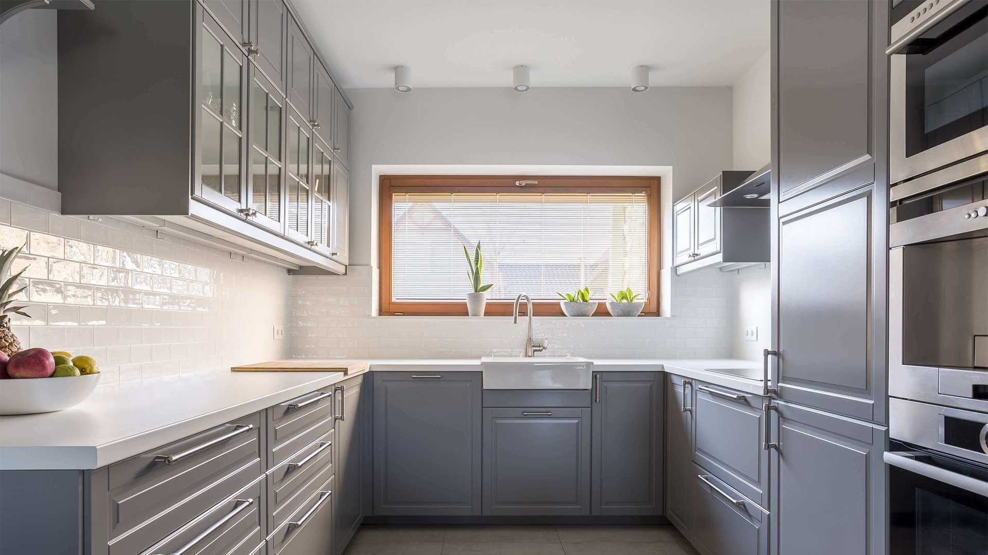 Modern kitchen with grey cabinets, white tile backsplash, and a wide horizontal hopper window above the sink.