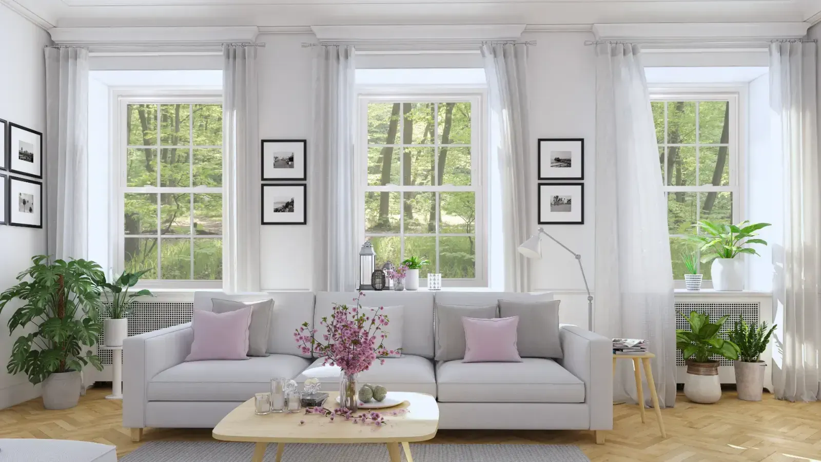 Bright, modern living room featuring a white couch with pink pillows positioned in front of three large double-hung windows framed by sheer white curtains and potted plants.