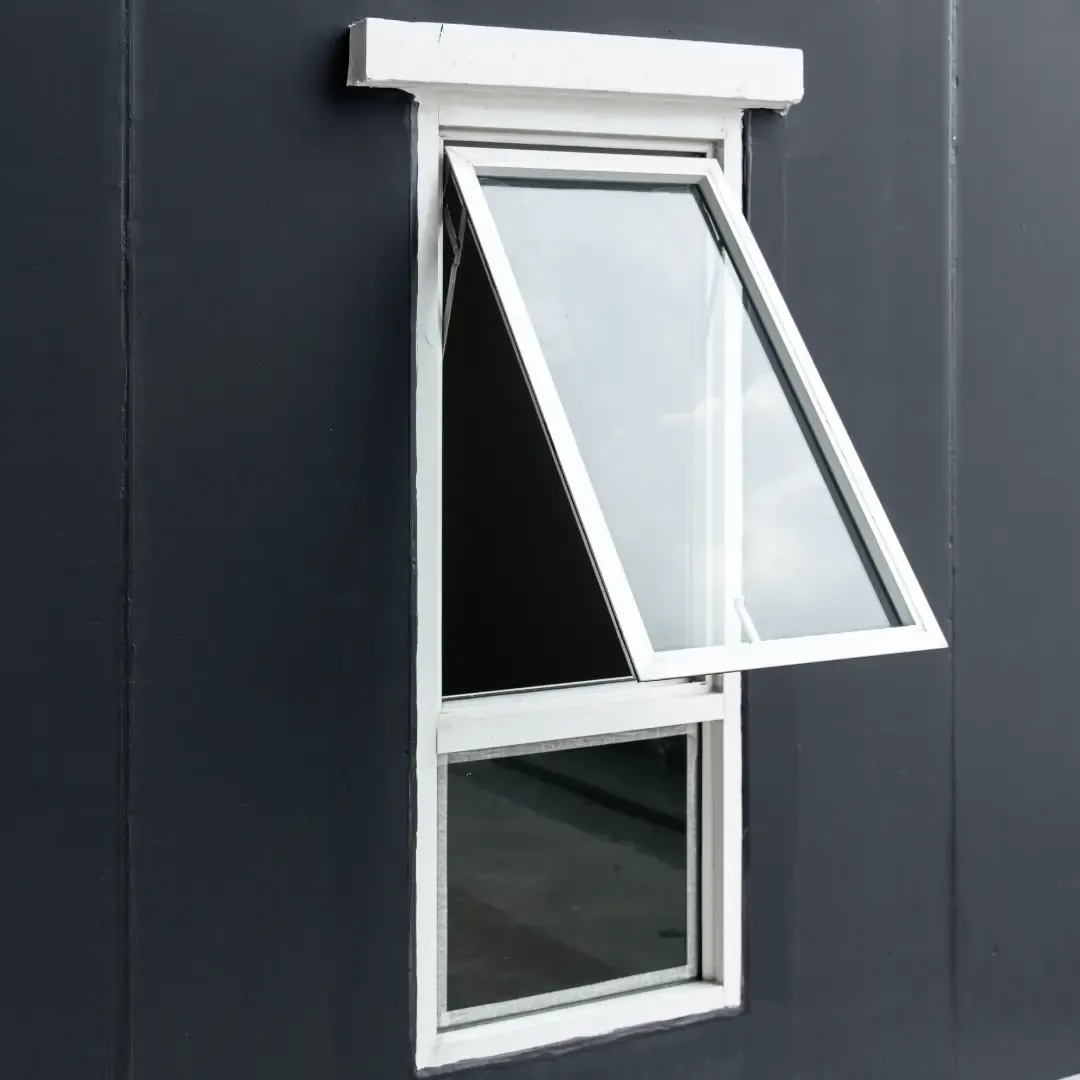 White vinyl awning window hinged at the top and opened outward, set against a dark grey wall above a lower stationary glass pane.