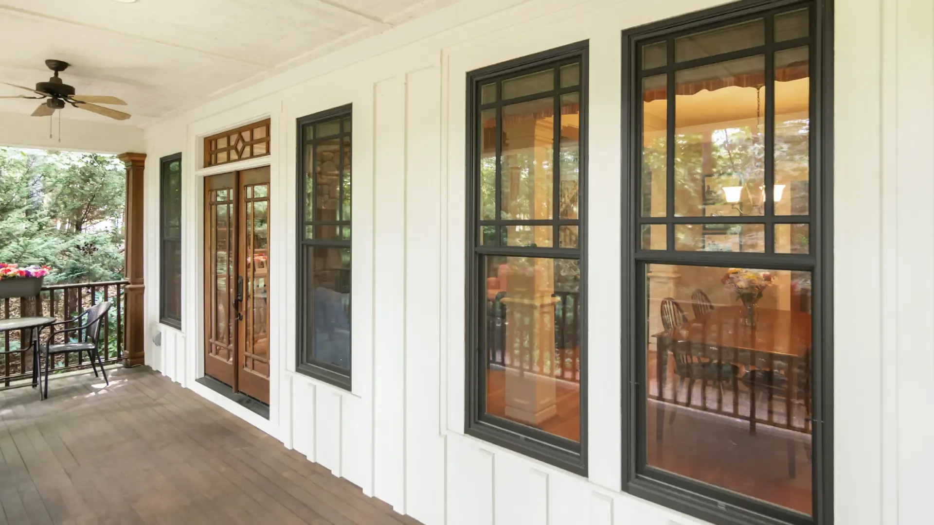Black double-hung windows with grilles on the upper sashes, installed along a white board-and-batten porch wall.