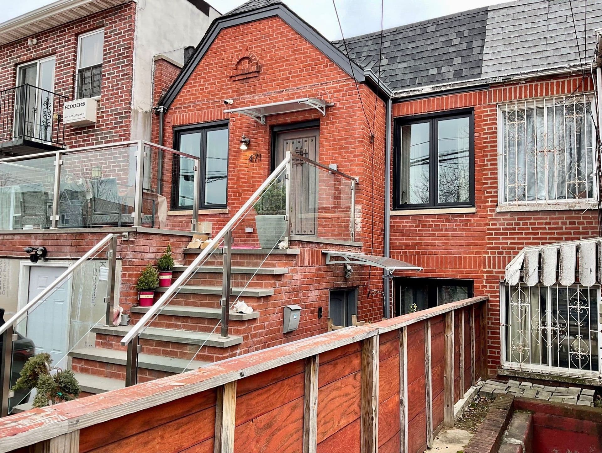 Exterior view of a red brick townhouse featuring new black-framed windows, glass panel railings on the front steps, and glass door awnings.