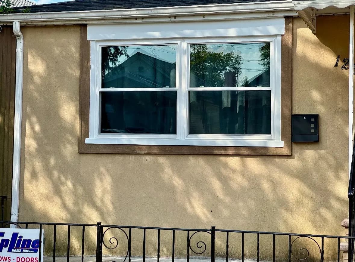 White double-hung vinyl window installed on a beige stucco wall with brown trim.
