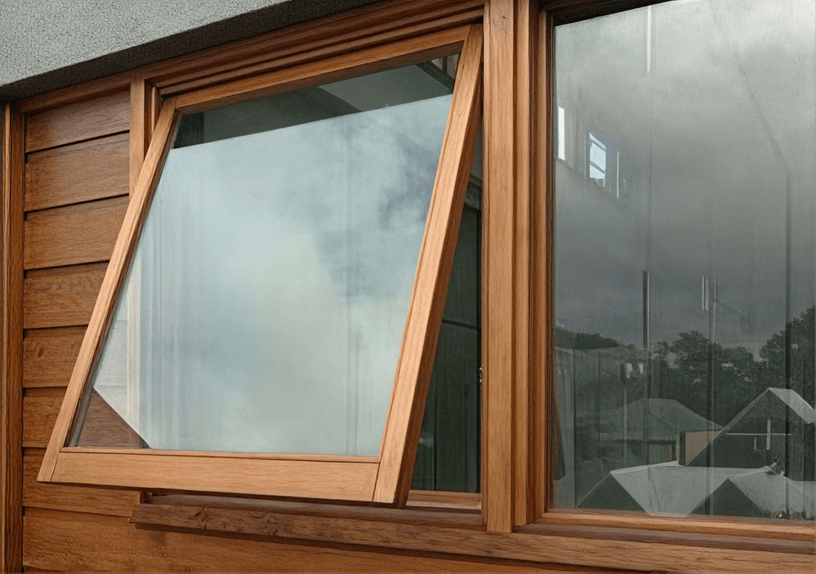 Exterior view of a wood-framed awning window pushed open from the bottom, set alongside a fixed picture window within a natural wood-finished exterior wall.