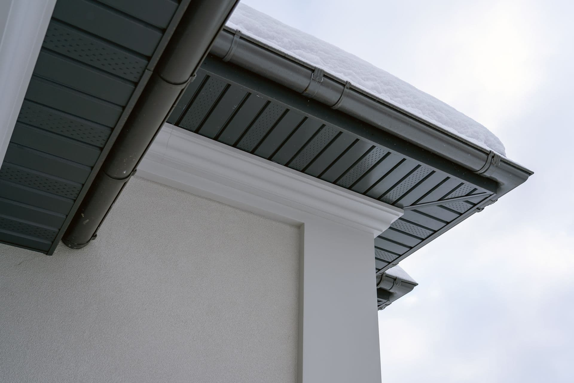 Corner of the house with new gray metal tile roof and rain gutter covered by snow at winter.