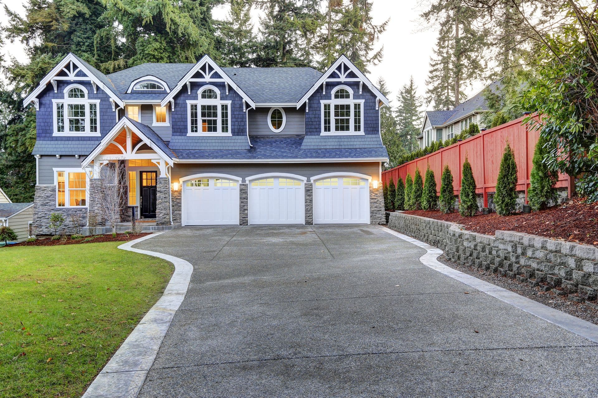 Luxurious home exterior with blue vinyl siding and white trim. Long concrete driveway lead to three attached garage spaces. Beautiful curb appeal. Northwest USA