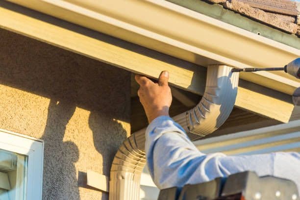 Worker installing gutter downspout on house exterior during home maintenance