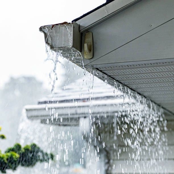 Ice dam with water and icicles hanging from residential gutter and downspout during winter freeze