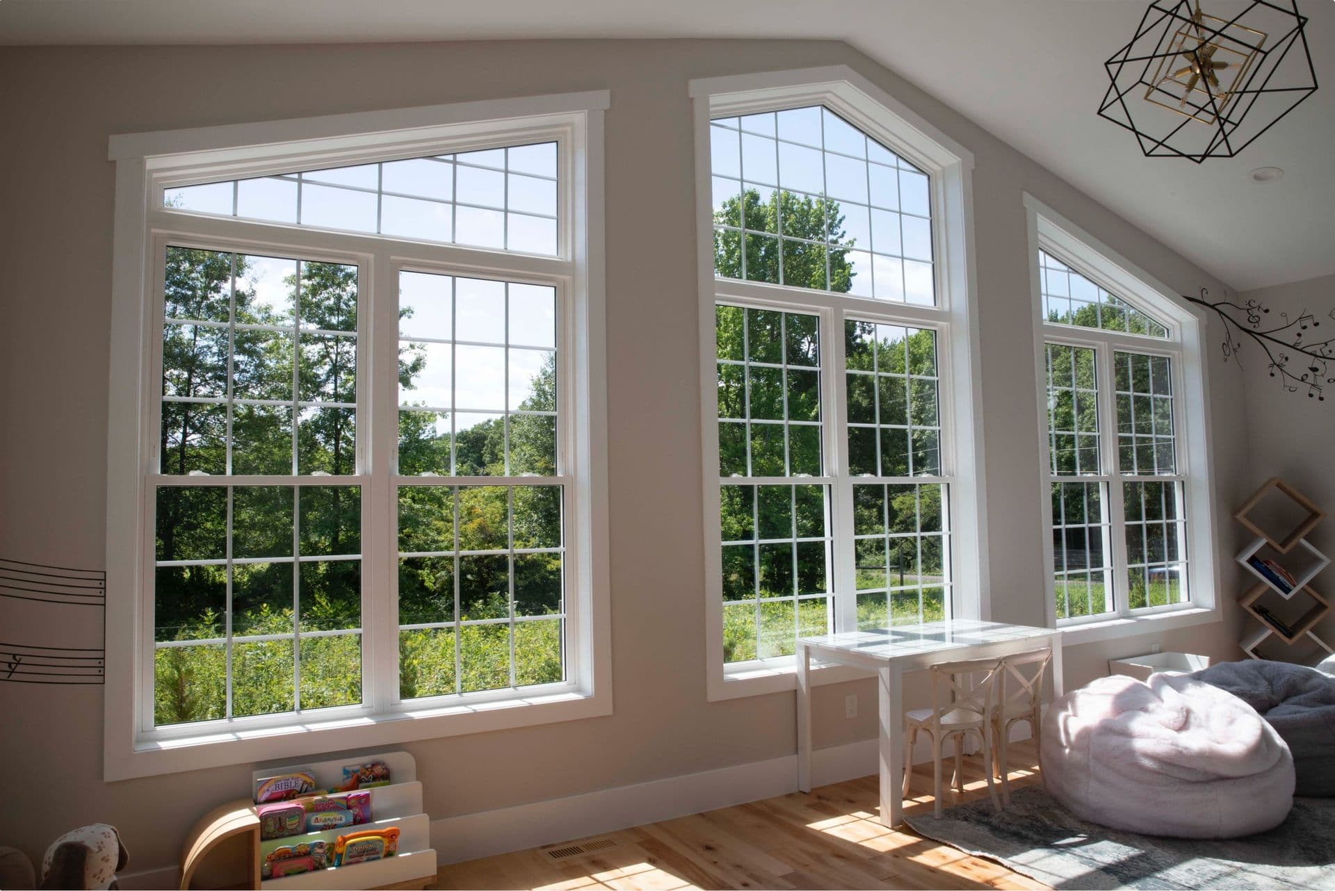 Large white-framed interior windows with grilles following the slope of a vaulted ceiling in a bright room with light hardwood floors and children's furniture.