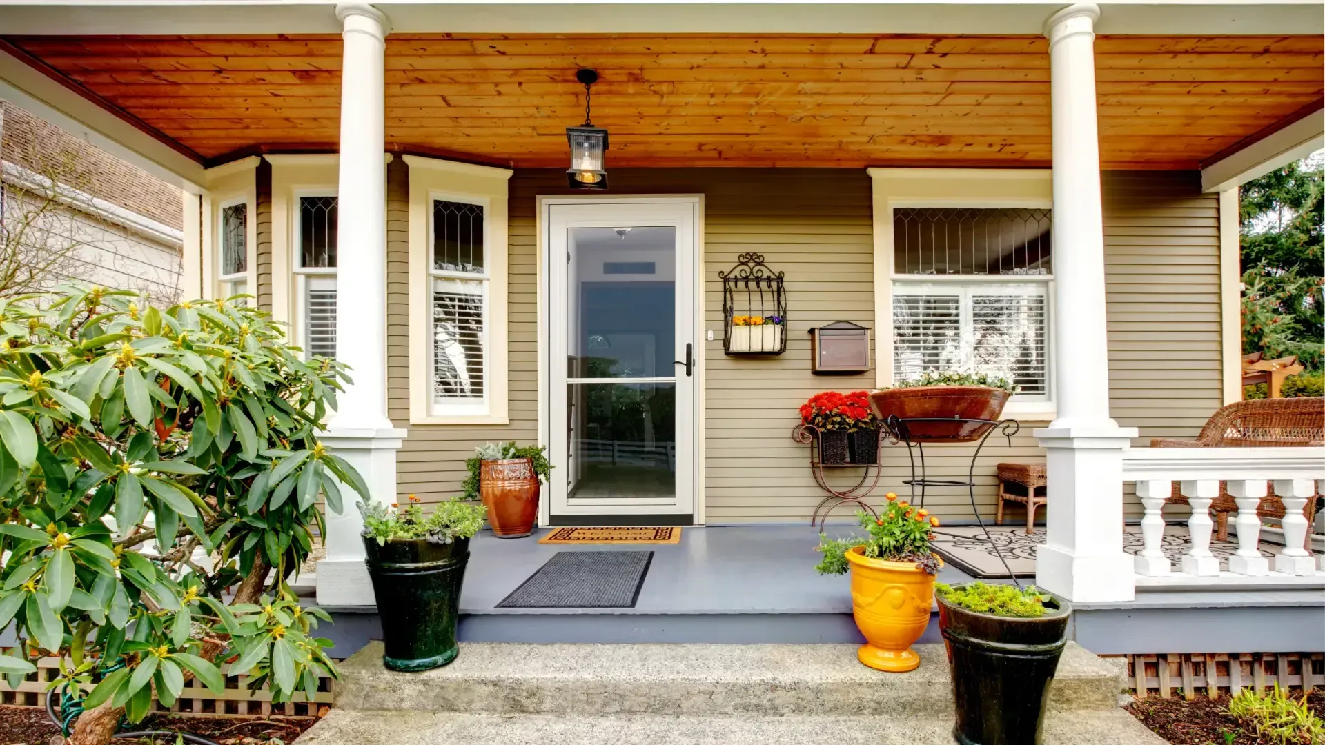 Exterior view of a white storm door with a full glass panel installed at the main entry of a covered porch with taupe siding and decorative planters.