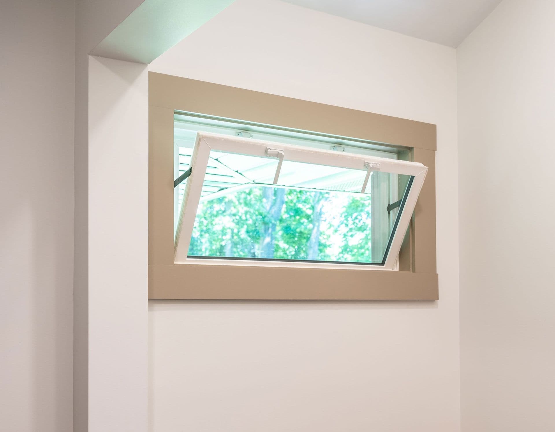 Interior view of an open hopper window with a white sash and latch hardware, framed by a thick tan-colored trim on a plain white wall.