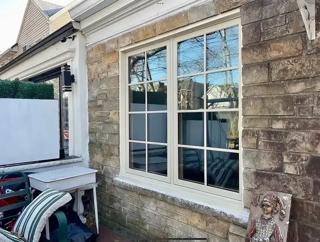 Exterior view of off-white double-hung windows with colonial grilles set into a stacked stone wall on an outdoor patio.