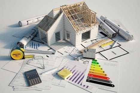 Architectural model of a house surrounded by blueprints, measuring tools, a calculator, and an energy-efficiency rating chart.