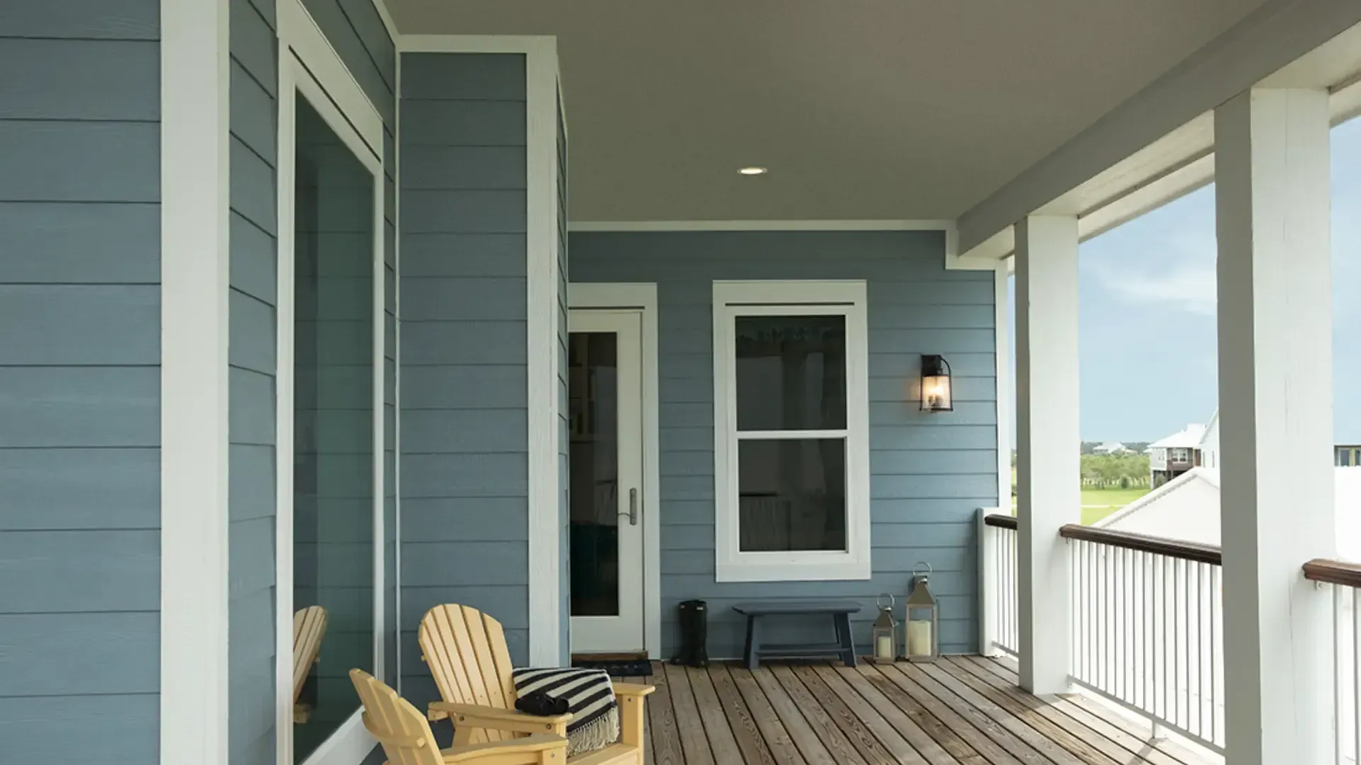 Covered porch with blue siding, white trim, wood decking, outdoor seating, and a glass entry door.