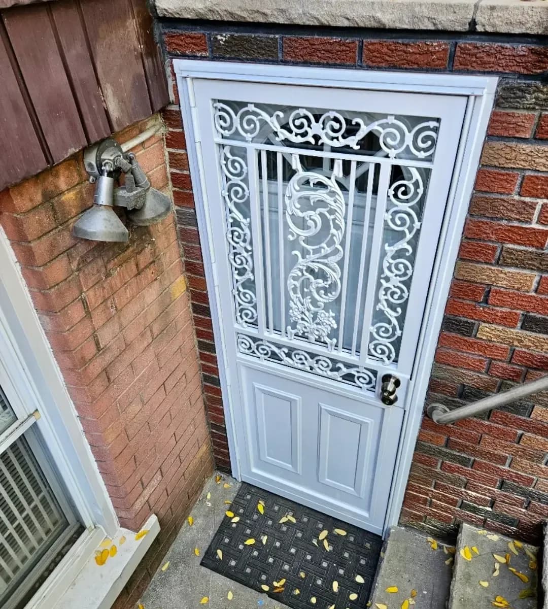 White decorative security door with ornate metal scrollwork installed in a red brick entryway.