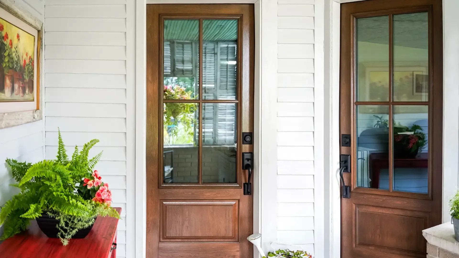 Two brown woodgrain entry doors with divided glass panels and black hardware on a white-sided porch.