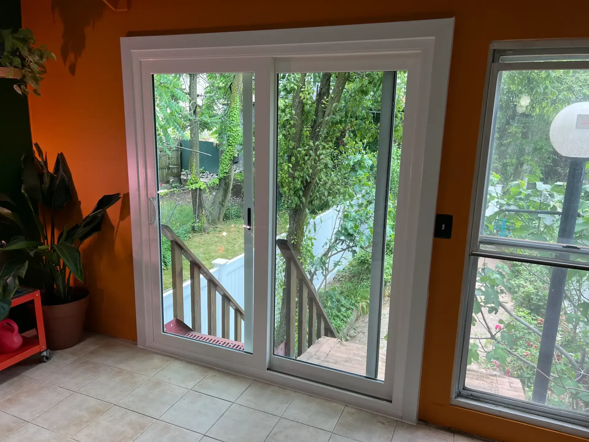 White-framed sliding glass patio door overlooking backyard steps, trees, and a white privacy fence.