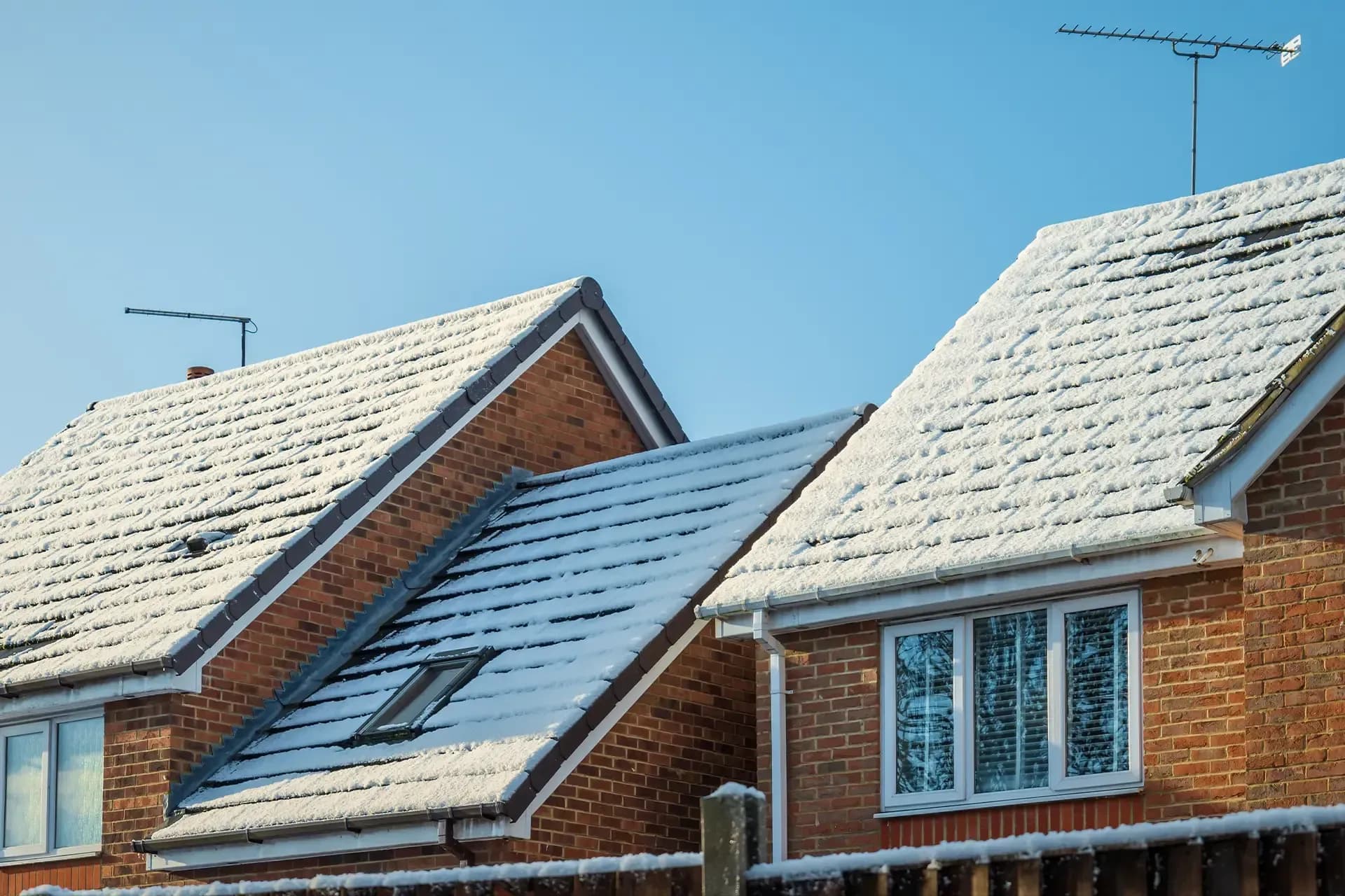 Snow-covered roofs of brick homes with white-framed windows, skylights, gutters, and rooftop antennas.