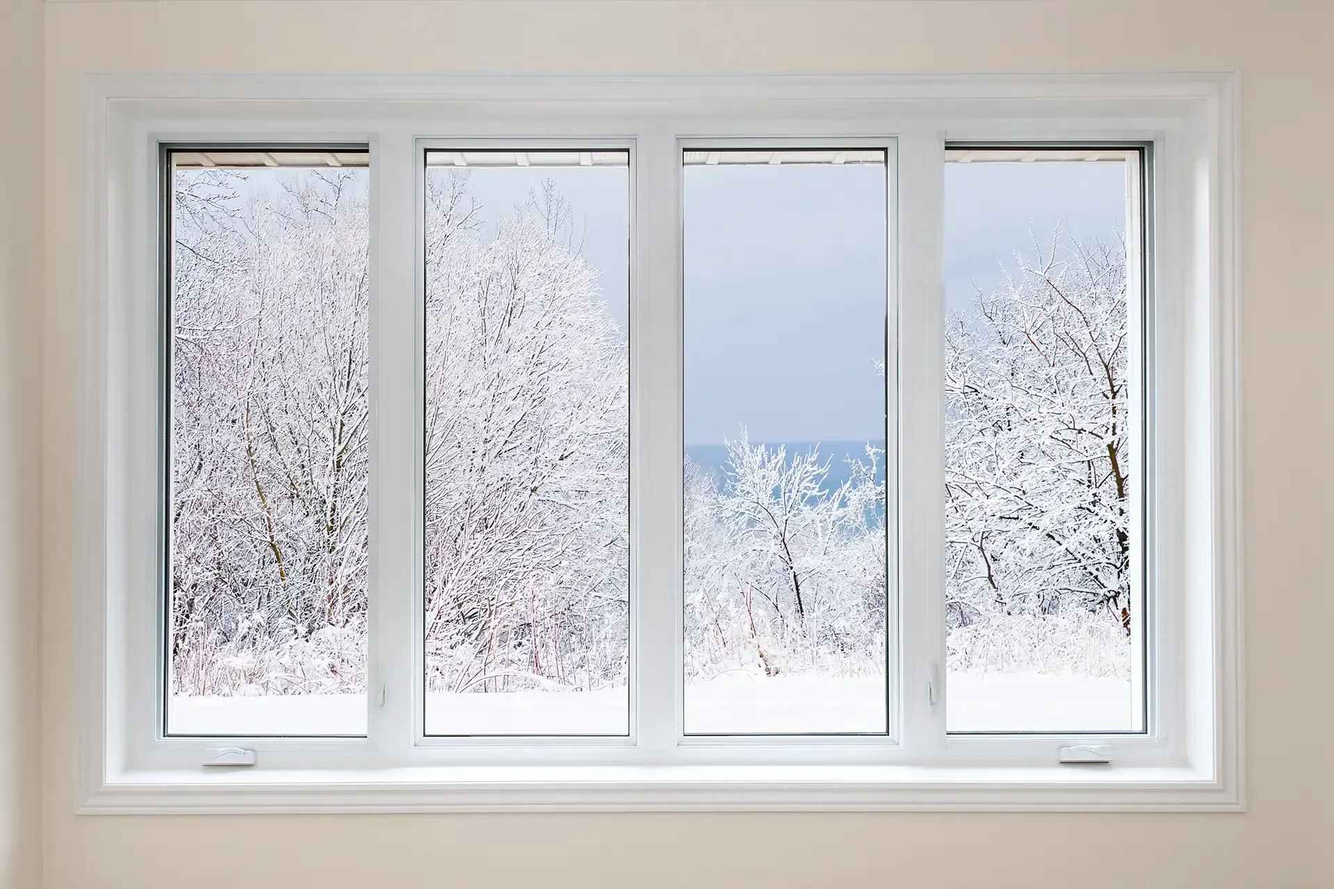 Four white-framed casement windows overlooking snow-covered trees and a winter landscape.