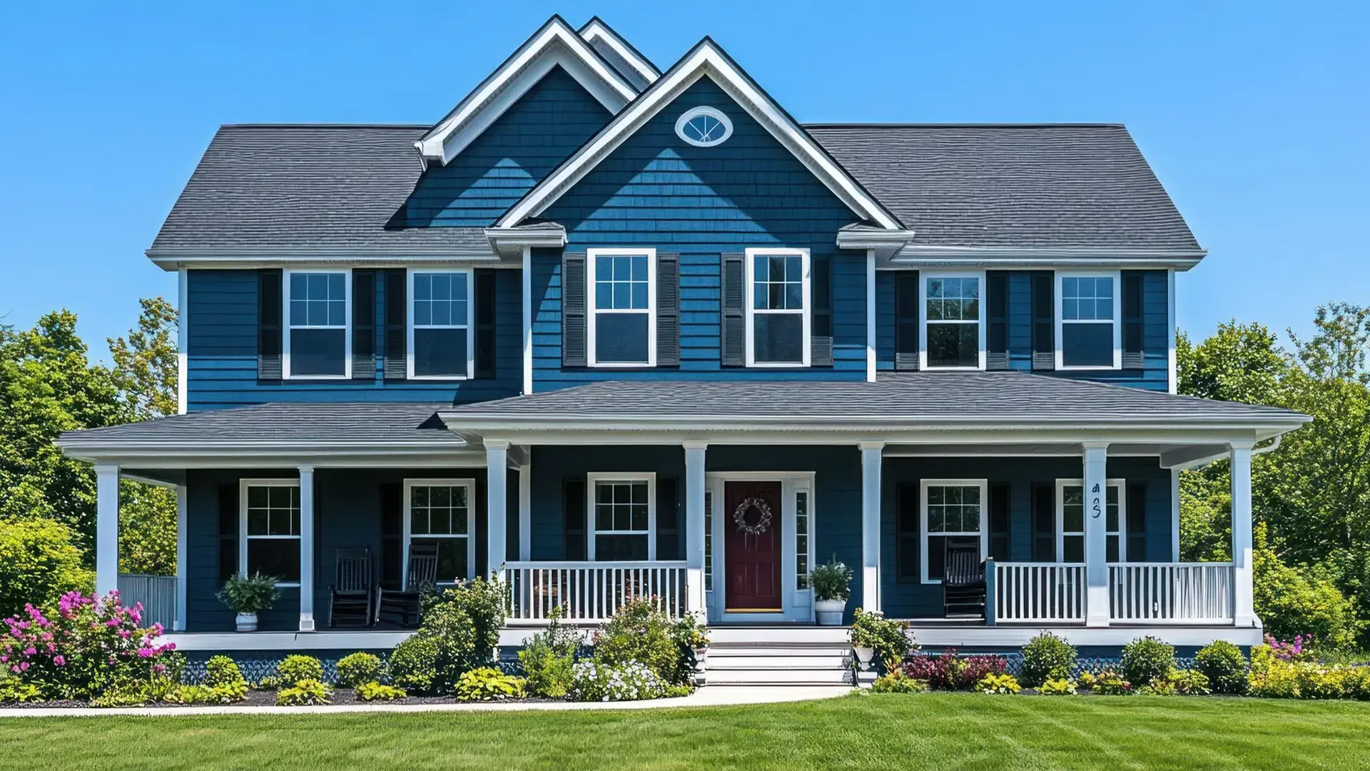 Large two-story home with dark blue siding, white trim, black shutters, a covered wraparound porch, and landscaped front yard.