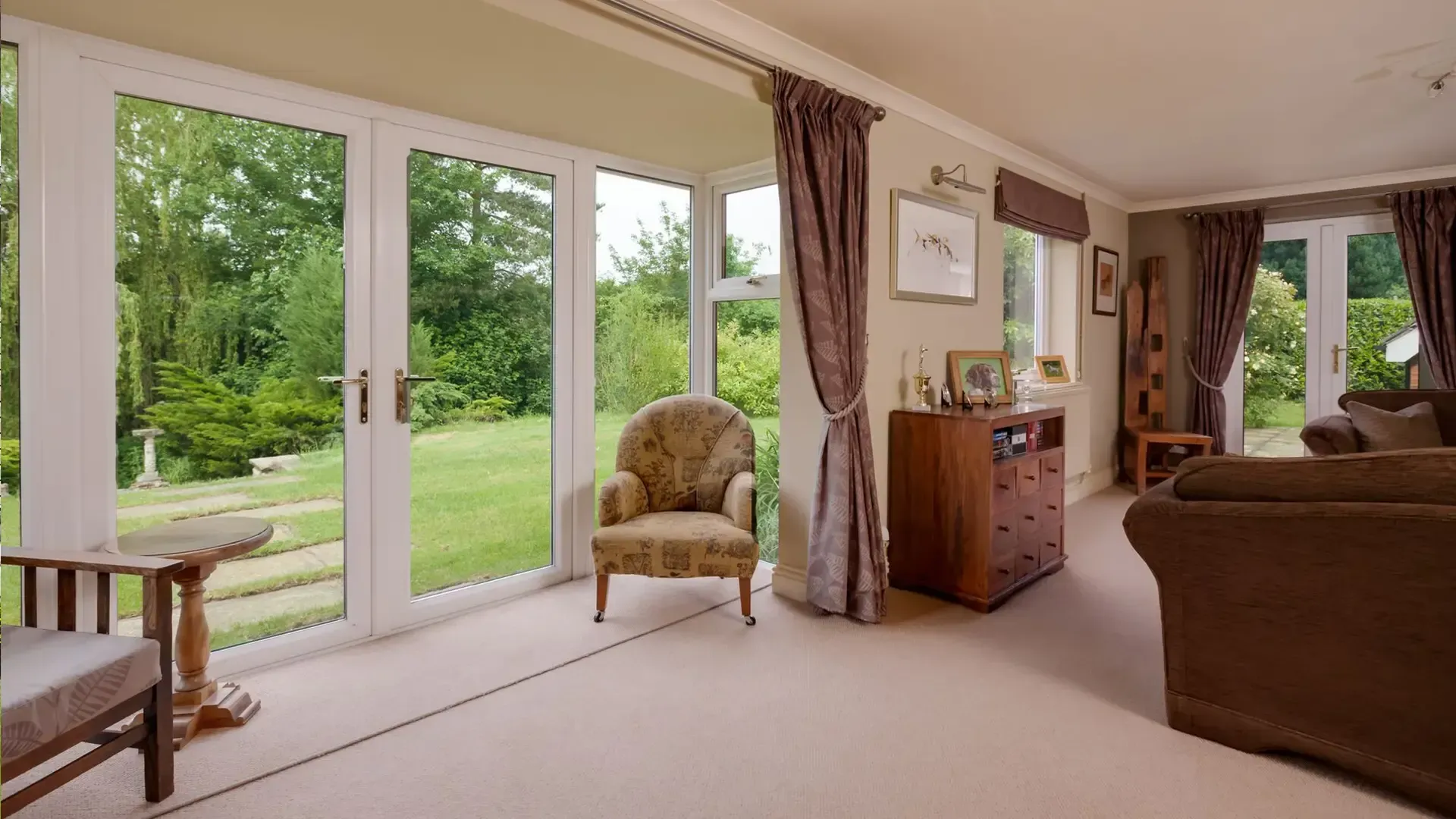 Bright living room with white-framed French patio doors and large windows overlooking a green garden.