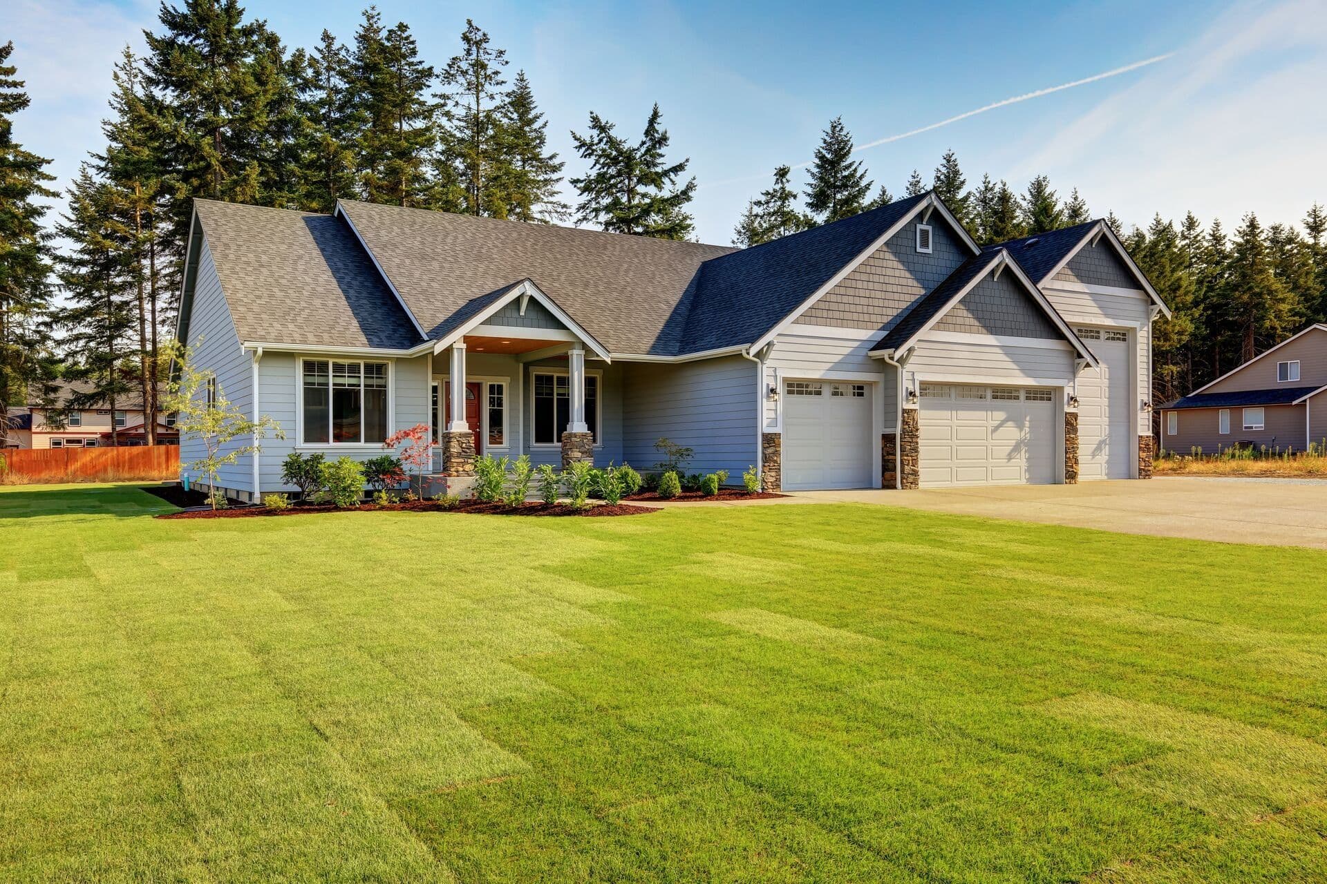 Large gray-sided home with a dark asphalt shingle roof, covered entry, three-car garage, and landscaped lawn.