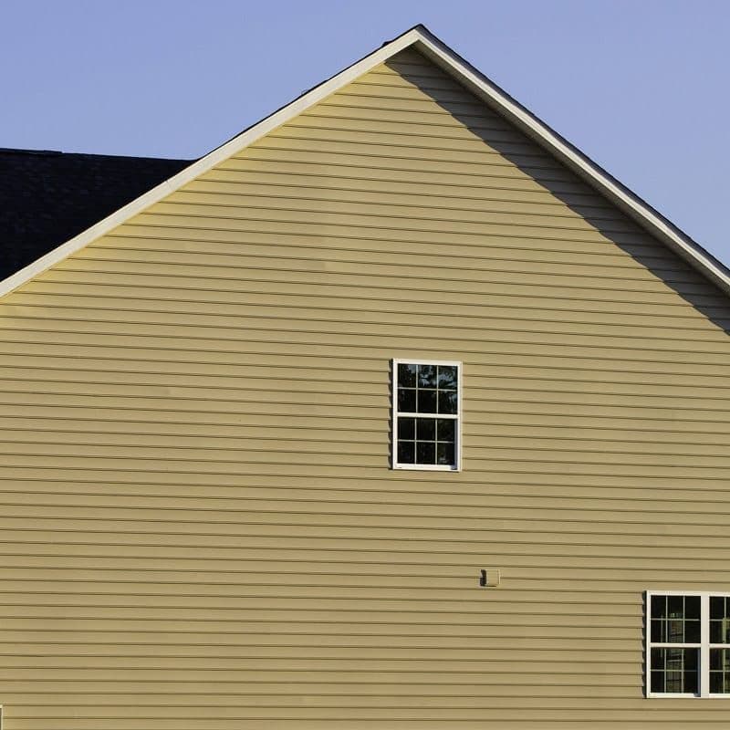 Side exterior of a home with beige horizontal siding, white trim, and small white-framed windows.