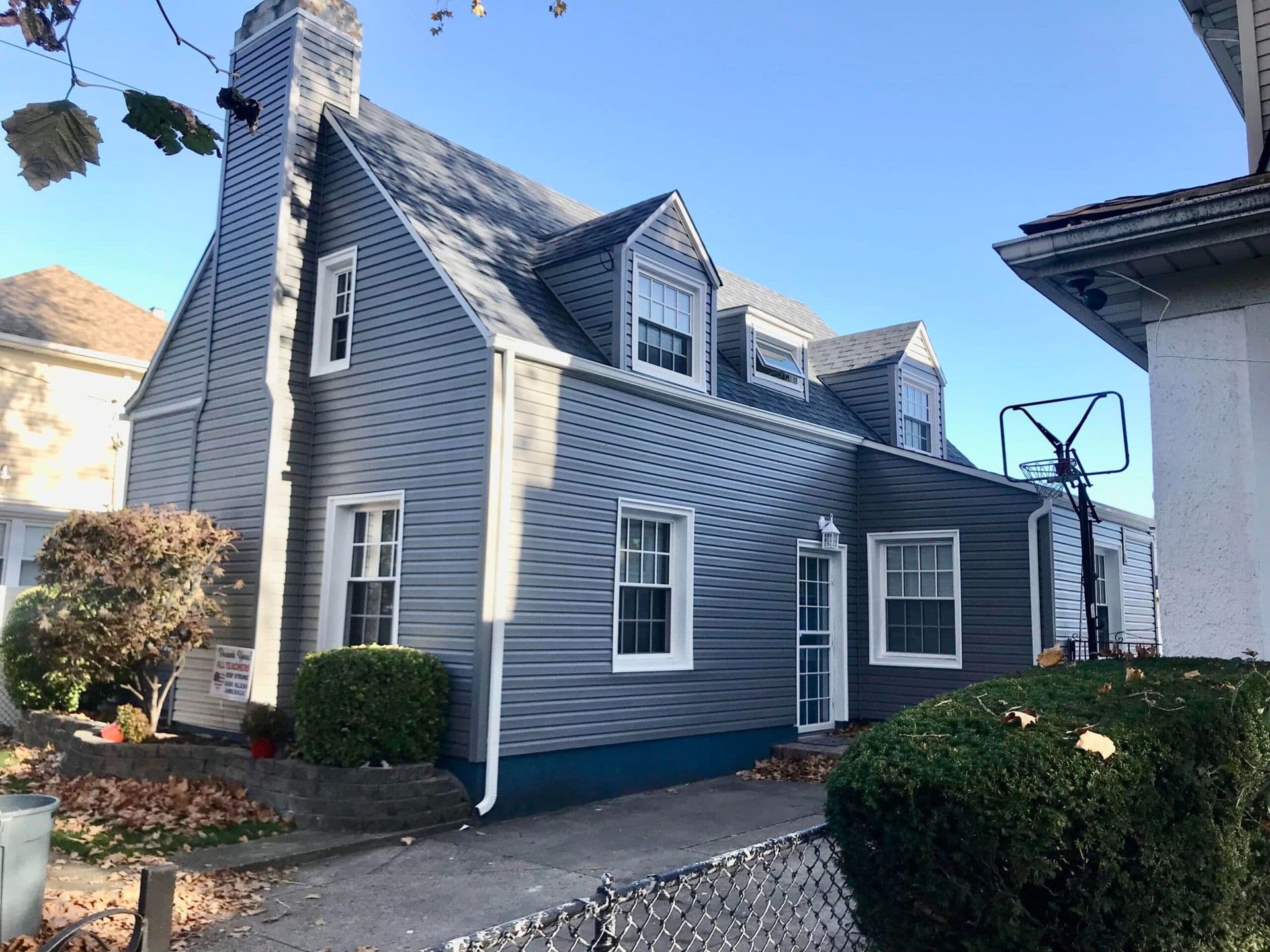 Gray-sided home with white-trimmed windows, dormers, a steep shingle roof, and an awning window.