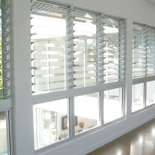 White-framed louvered windows with adjustable glass slats overlooking a bright outdoor patio.