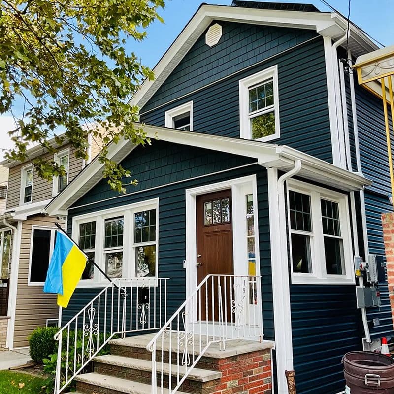 Dark blue two-story home with white trim, replacement windows, a brown front door, brick steps, and a Ukrainian flag.