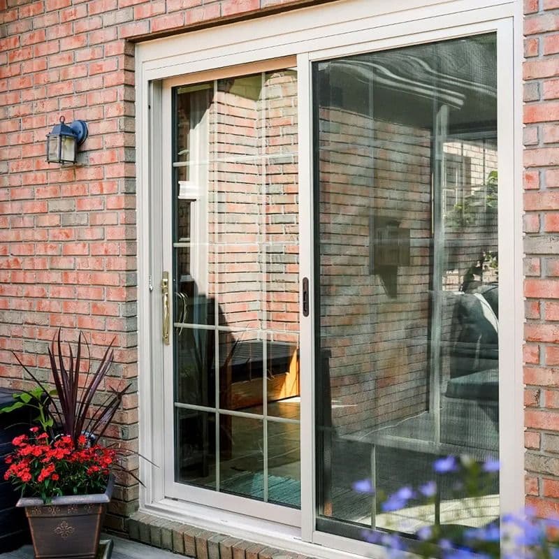 White-framed sliding patio door installed in a red brick wall with decorative flower planters.