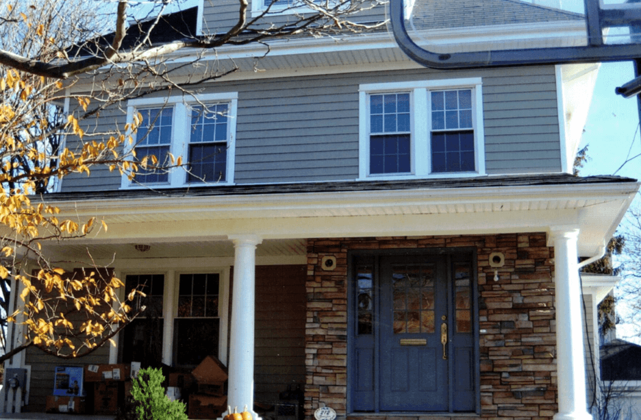Two-story home with grey siding, a stone entryway surround, and double-hung windows behind a front porch.