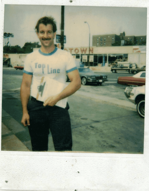Worker in a Top Line t-shirt holding a clipboard outside near a street.
