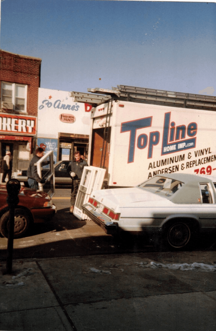 Top Line crew unloading replacement windows from a work truck parked on a city street.