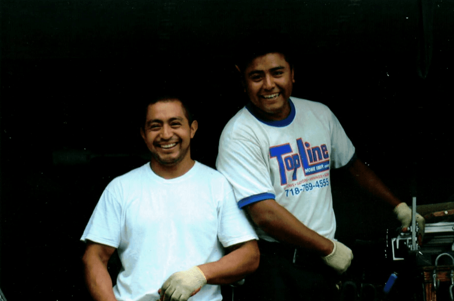 Two smiling contractors wearing work gloves and a TopLine t-shirt outdoors.